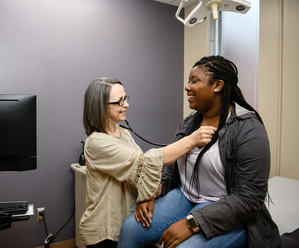 Medical provider at Redfern Health Center listens to a patient's pulse as the patient sits on the exam room table