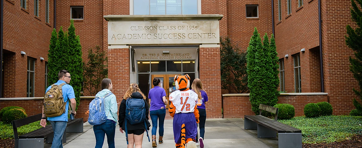 A group of students and a tiger mascot are walking towards the Clemson Academic Success Center.
