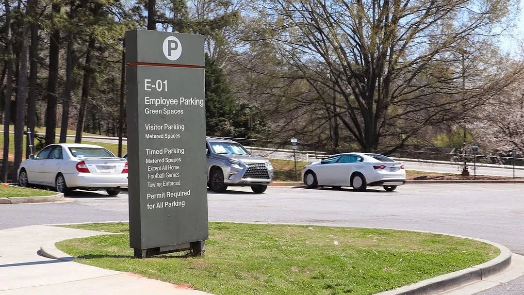 A sign designates E-01 parking for employees, visitors, and timed parking, with several cars in the background.
